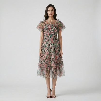 Model wearing the Amy Floral Midi Dress in light pink and green tiered tulle with an off-the-shoulder ruffled neckline.