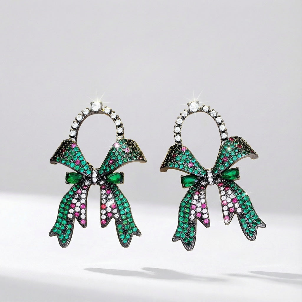 A pair of Amyla bow-shaped earrings made of copper with green cubic zirconia rhinestones on a clean studio background