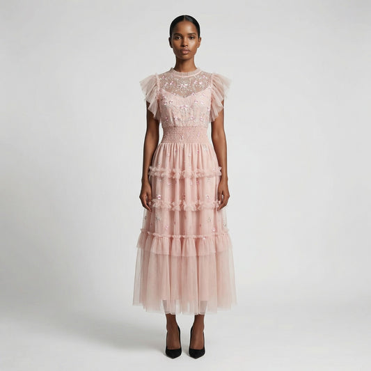 Full-length view of the Domenica pink mesh maxi dress featuring white and pink floral embroidery, a smocked waistline, and a tiered ruffled skirt laid out on a white faux fur rug.