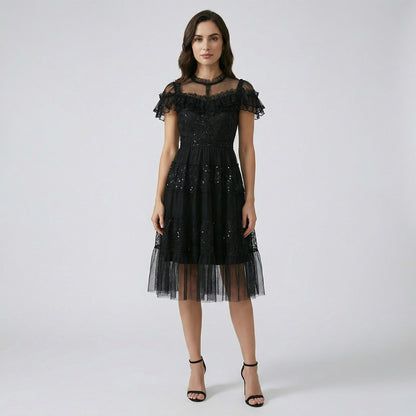 Model wearing Flavia black sequin tulle dress with tiered skirt and ruffled lace neckline.