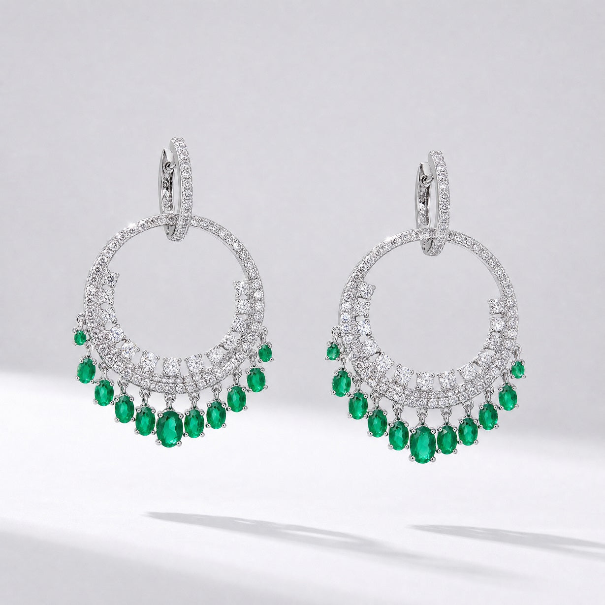 Pair of silver Laura tassel earrings featuring a circular cubic zirconia hoop with green emerald-colored water drop charms hanging from the bottom.