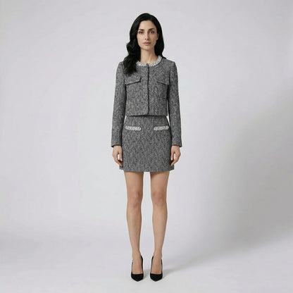 Front view of Susan two-piece herringbone tweed set featuring a crystal-embellished collarless jacket and matching mini skirt on a cream sofa.