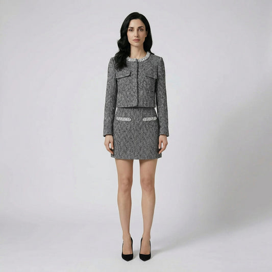 Front view of Susan two-piece herringbone tweed set featuring a crystal-embellished collarless jacket and matching mini skirt on a cream sofa.