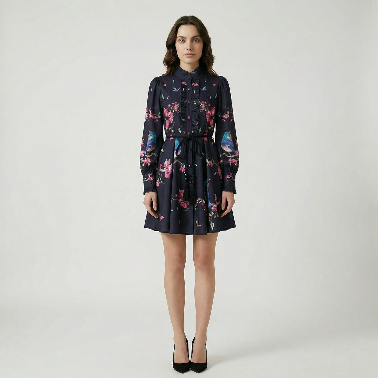 A ruffled mini dress named Suzanne featuring a print of blue birds, pink blossoms, and butterflies, shown in black and cream color options.