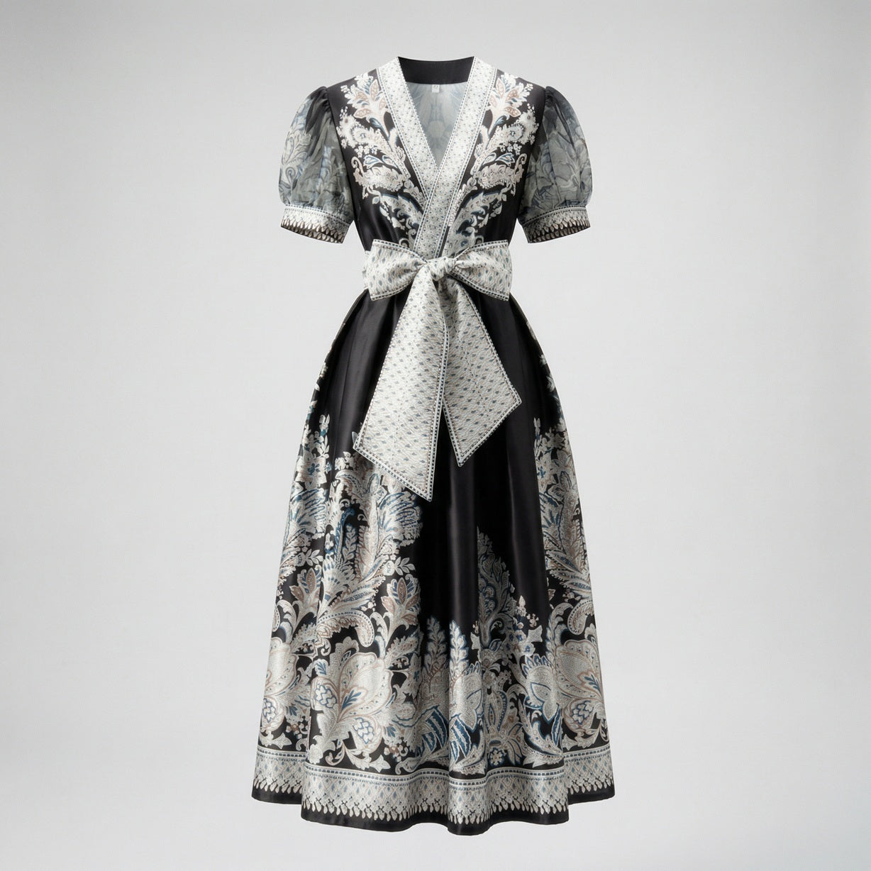 Two Teodora maxi dresses in black and white featuring paisley prints, puff sleeves, and large bow belts.